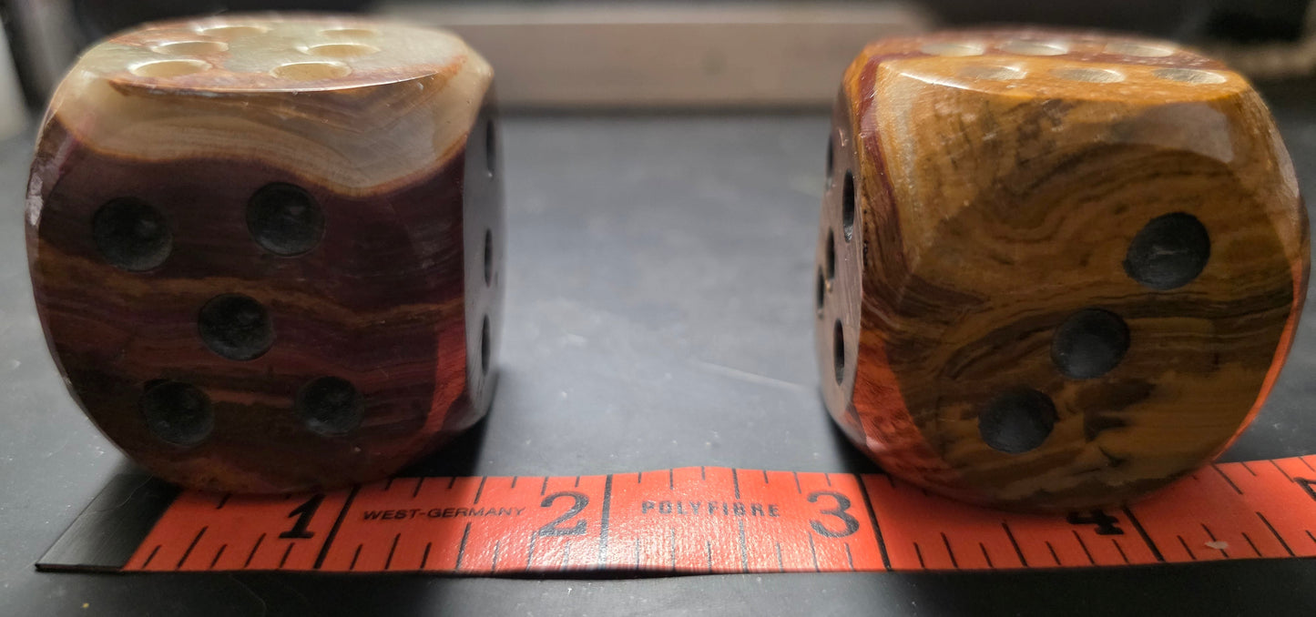 Two onyx dice with a measuring tape showing their size on a dark surface.