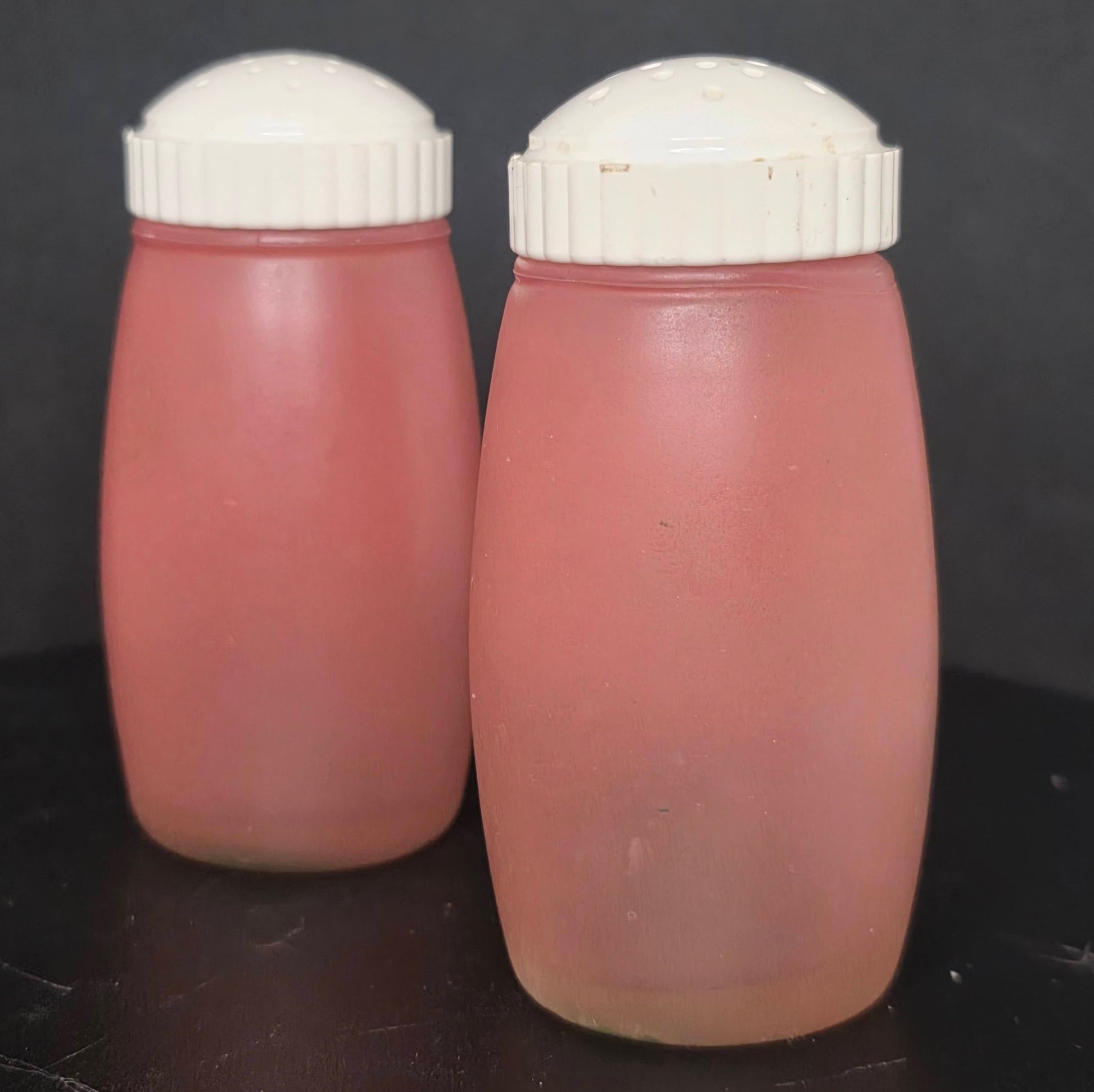 Back view of vintage Bartlett Collins pink frosted glass shakers showing plastic lids