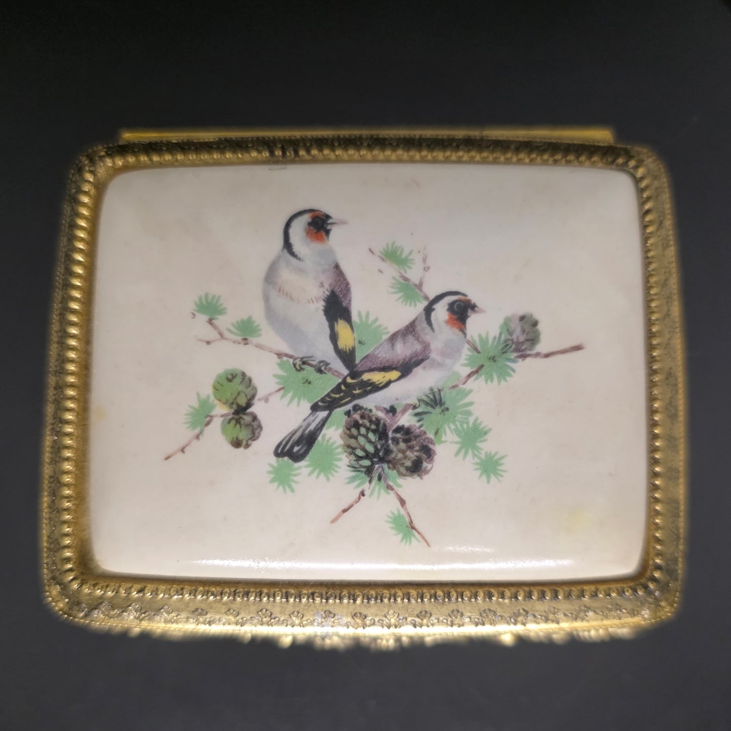 Close-up of enamel mockingbird and pine branch artwork on vintage Sankyo music box
