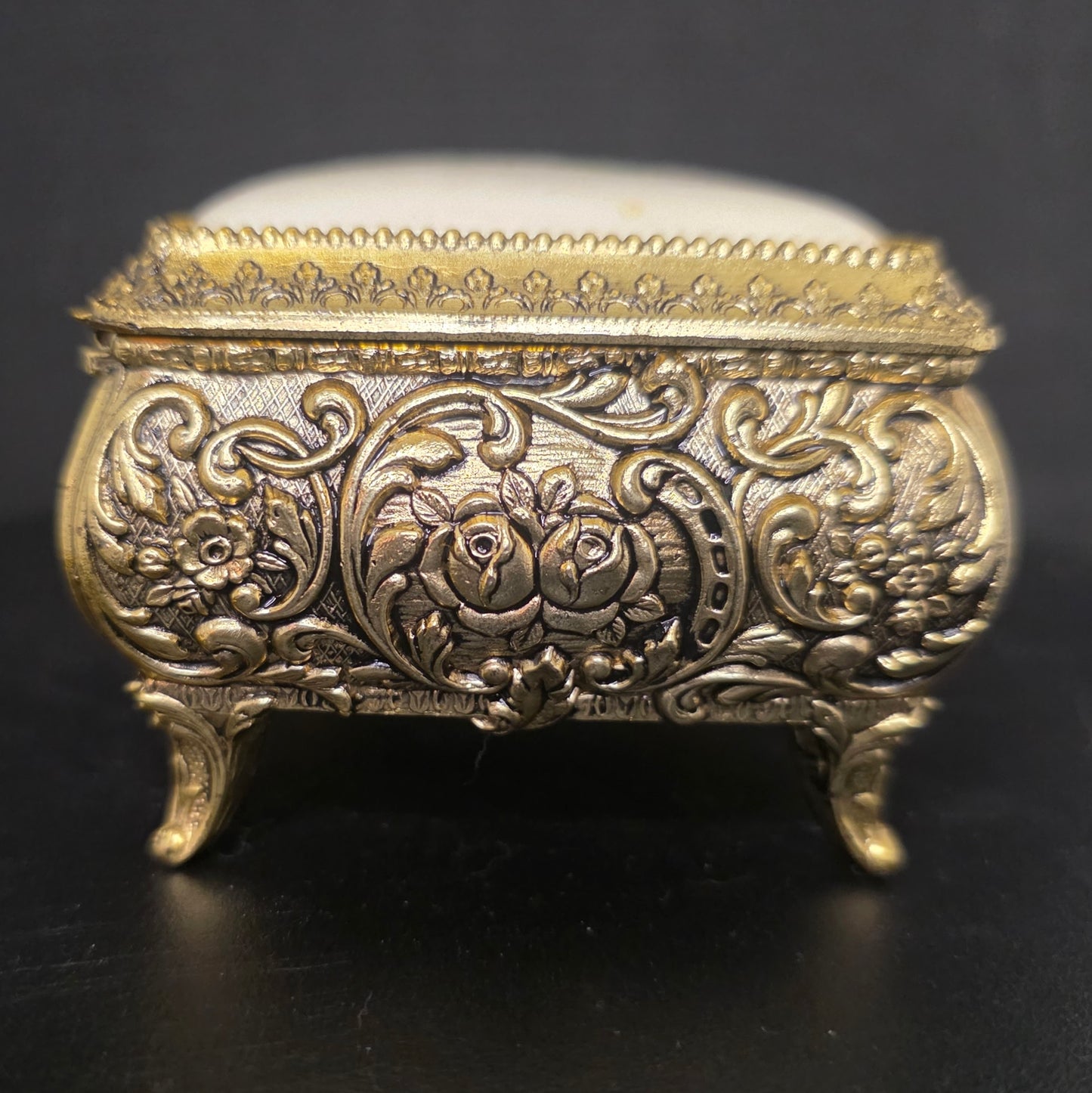 Side view of ornate brass trinket box with embossed filigree and floral details