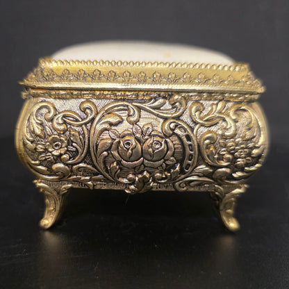 Side view of ornate brass trinket box with embossed filigree and floral details