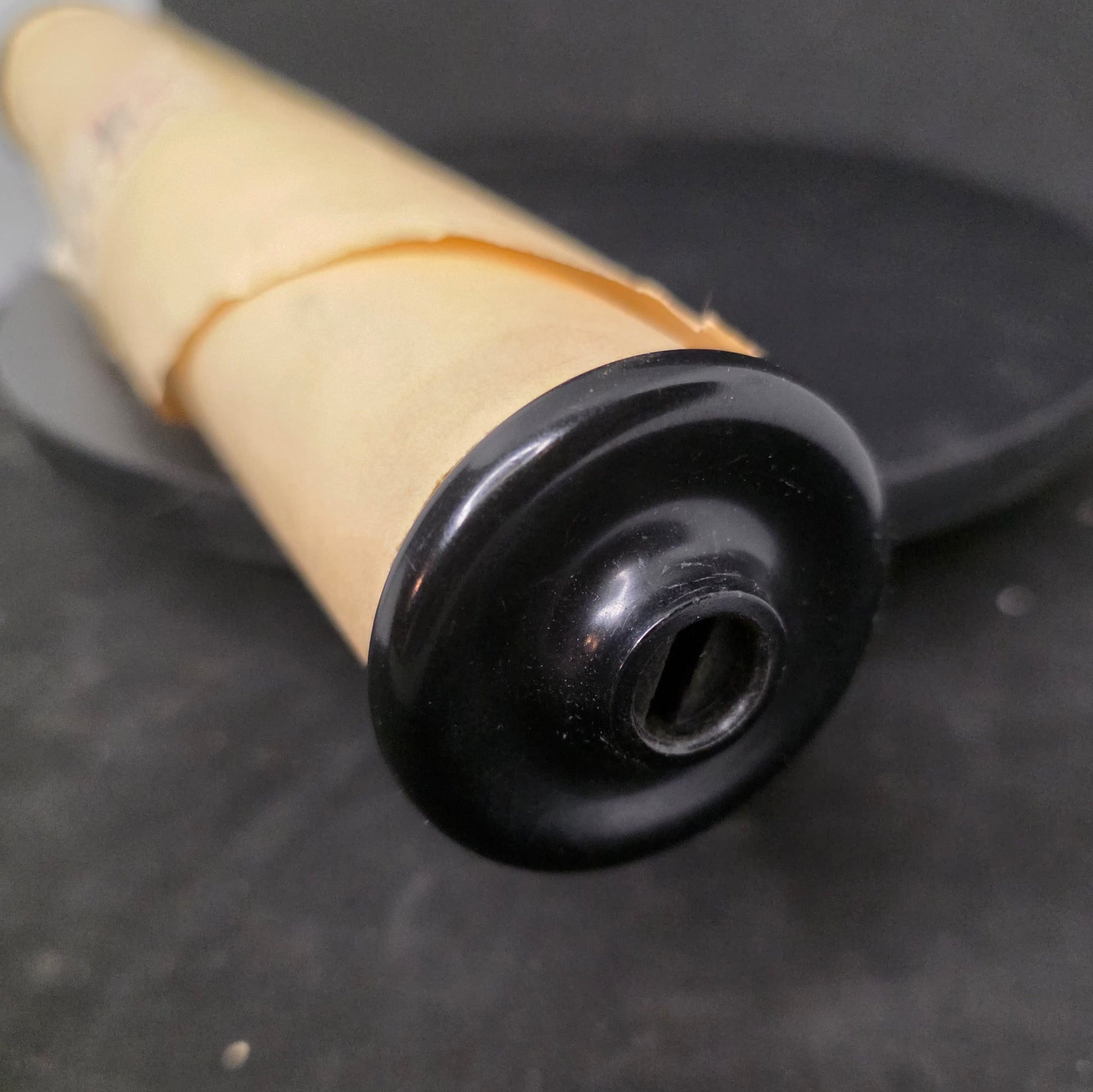 Close-up of black Bakelite flanged end cap on vintage Q.R.S MICKEY piano roll showing authentic period hardware