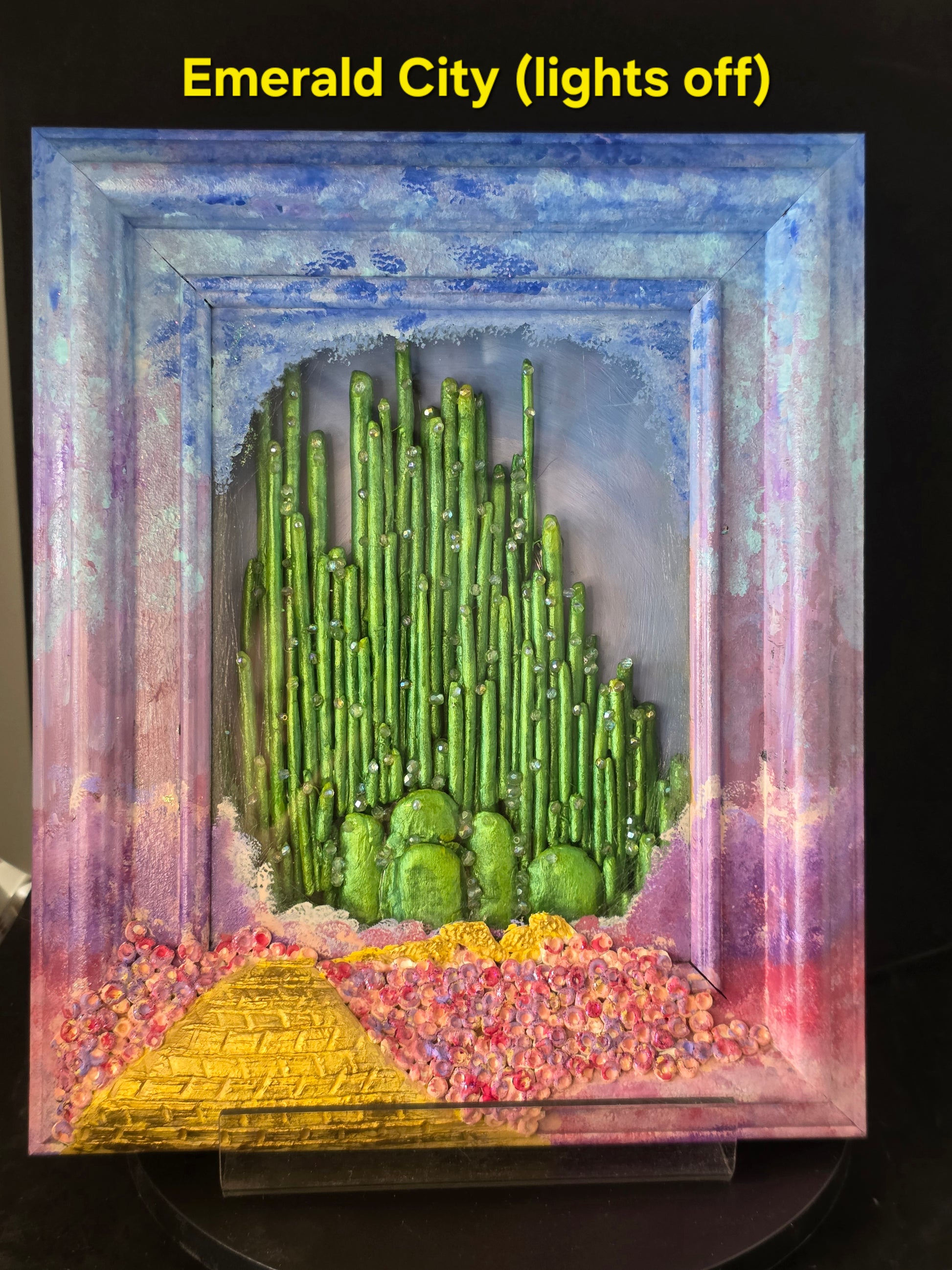 Wizard of Oz Emerald City original shadow box art — lights off, showing hand-painted ombre sky, yellow brick road, poppy fields, and clay spire Emerald City