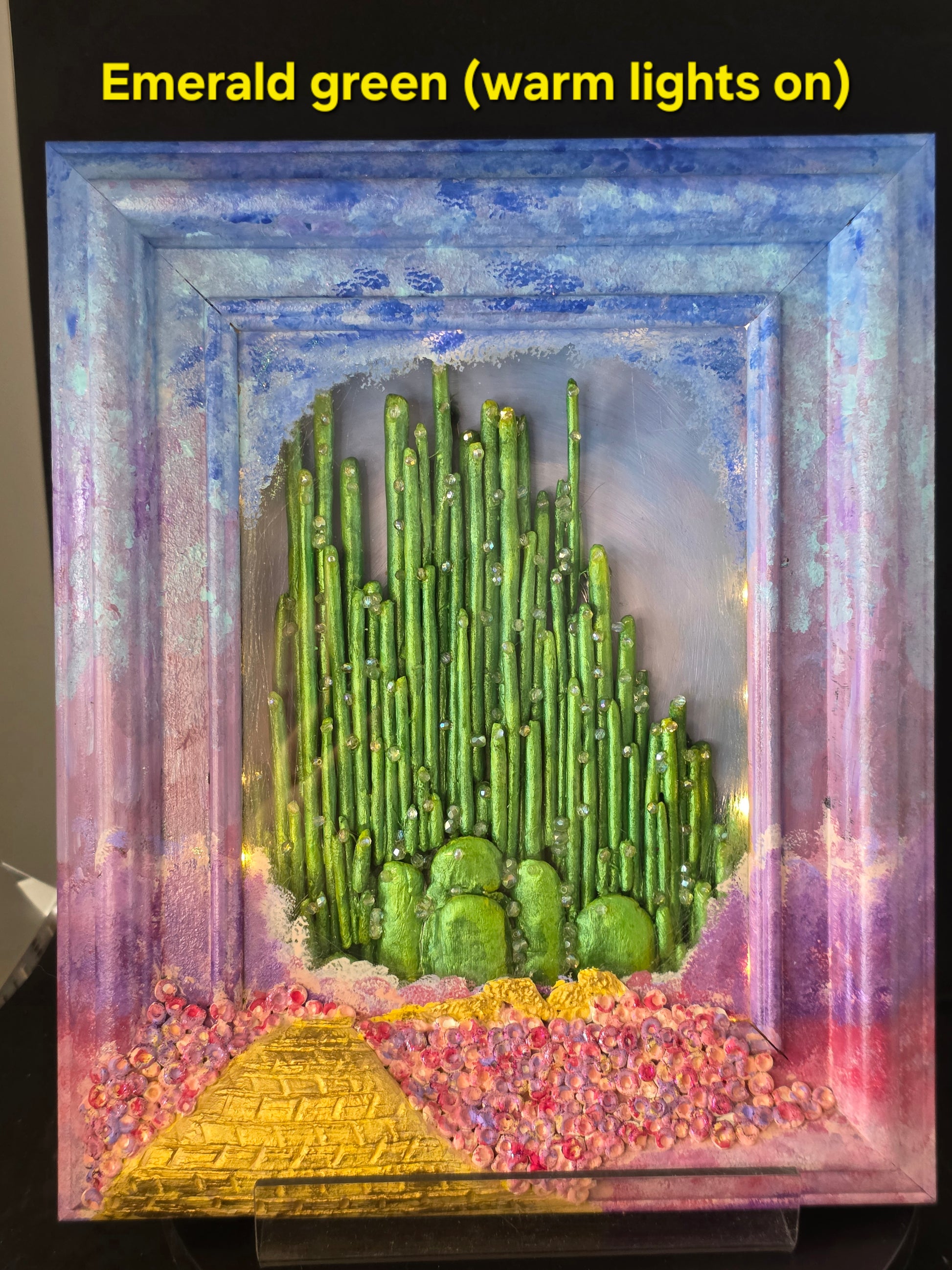 Wizard of Oz Emerald City shadow box with warm white fairy lights illuminated behind glass, casting a soft golden glow
