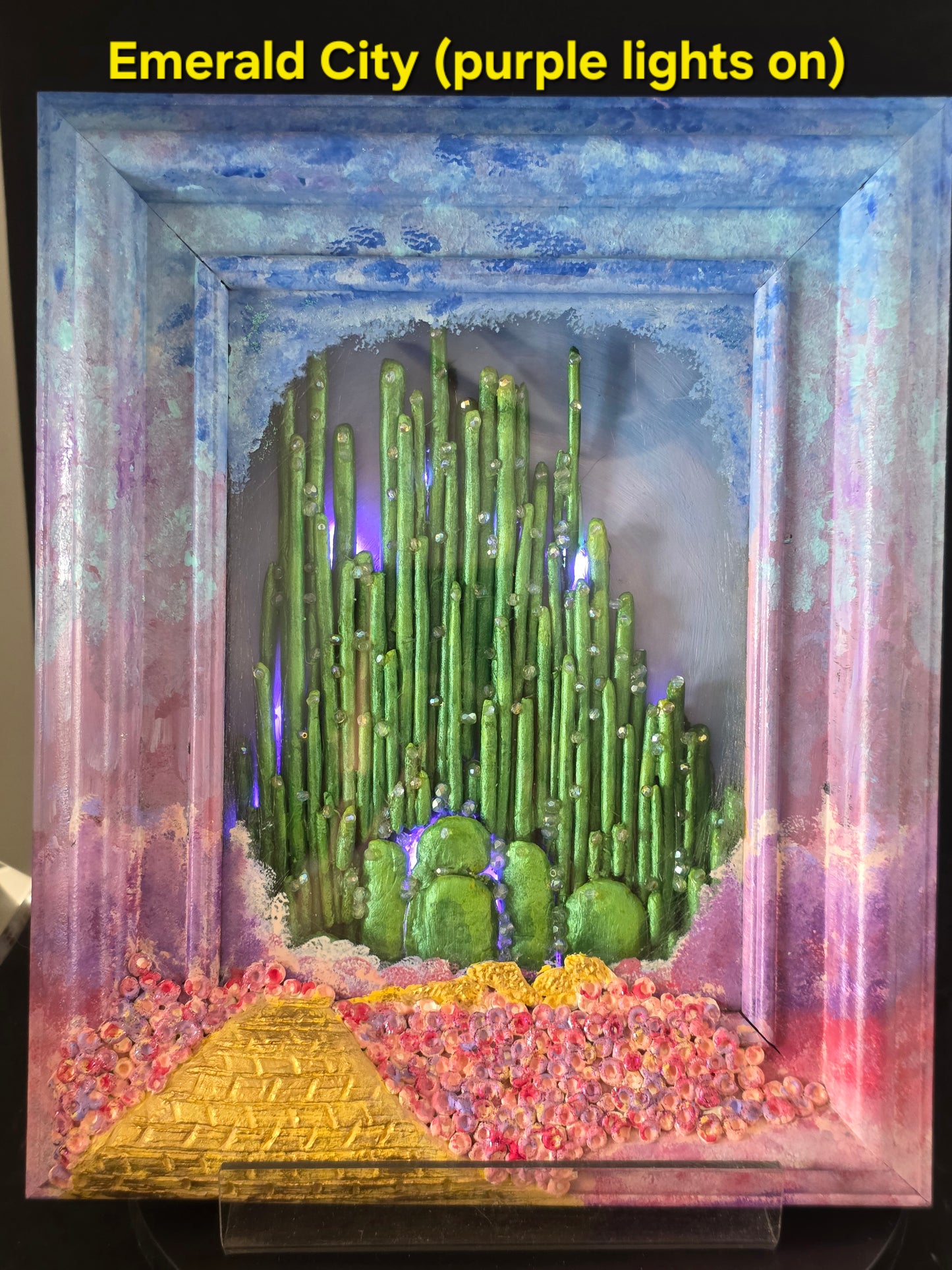 Wizard of Oz Emerald City shadow box with purple fairy lights on, highlighting the iridescent bead details and clay spires in violet light