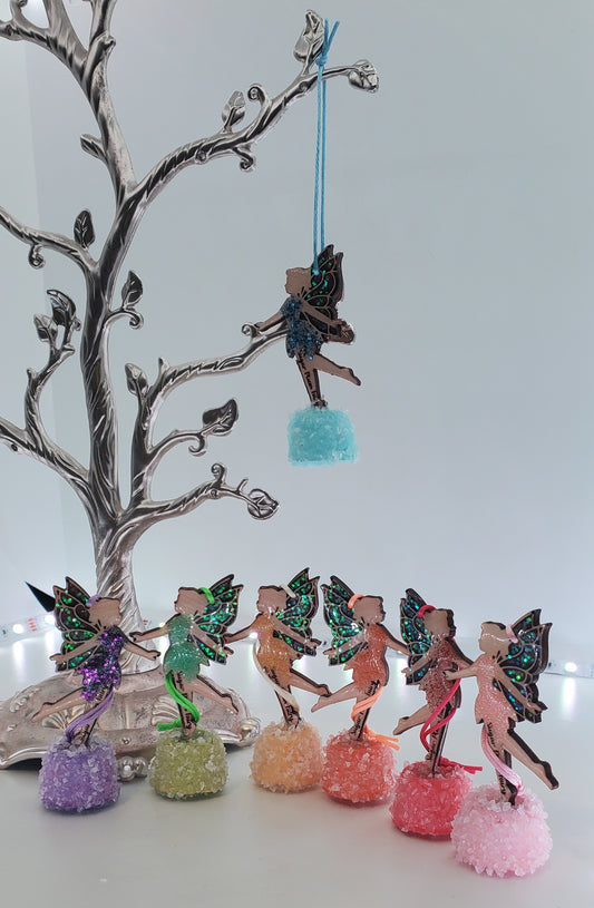 Set of colorful fairy figurines on decorative bases with a tree branch in the background.