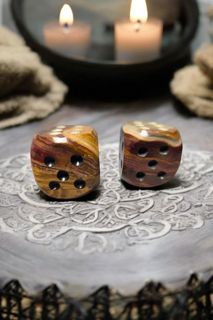 Two onyx dice on a textured surface with candles in the background