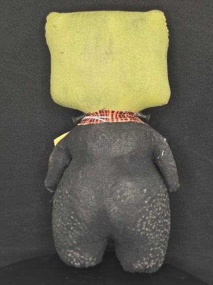 Backside of a handmade Frankenstein doll, shown on a dark background.
