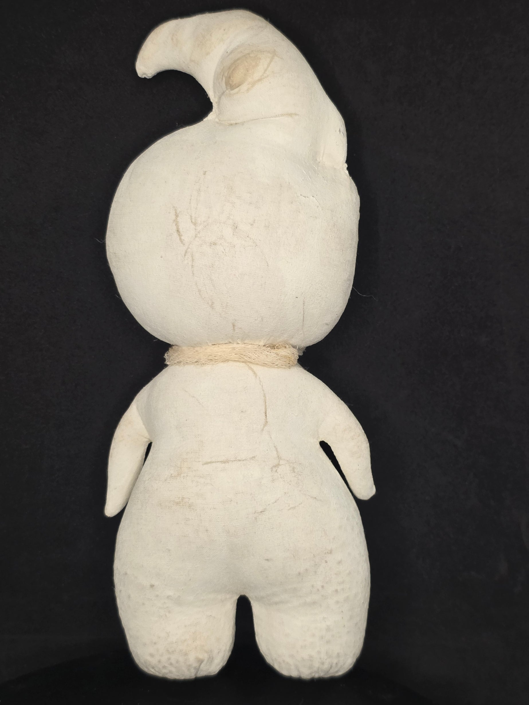 Backside of a ghost doll photographed from above on a black background.