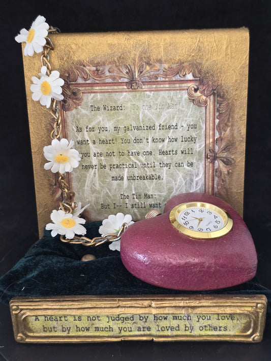 Wizard of Oz Tin Man's Heart working clock mixed media art — heart-shaped ceramic resin clock with stainless steel and gold daisy chain, displayed on a gold metallic acrylic stand with movie quote, dark green velvet cushion, full display view