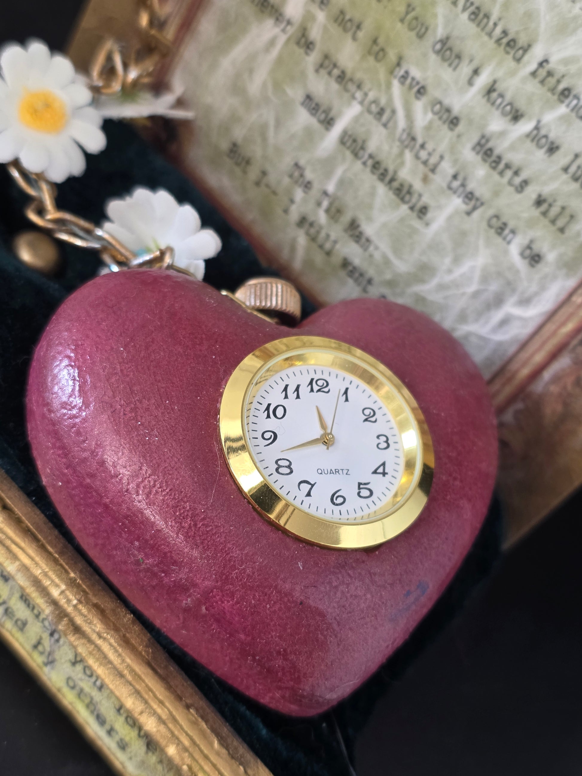 Close-up of the Tin Man's Heart clock — heart-shaped eco-friendly ceramic resin with functioning mini clock face, gold daisy chain detail, and UV resin seal finish