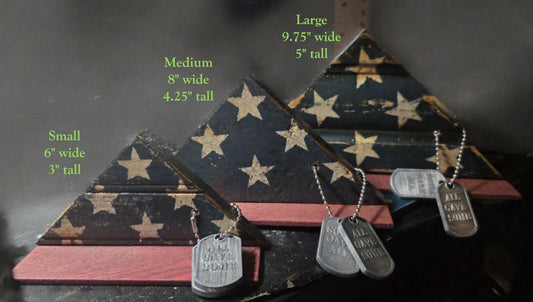 Three sizes of handcrafted Tribute Memorial Flags made from reclaimed wood — Small (6"×3"), Medium (8"×4.25"), and Large (9.75"×5") — displayed side by side, each with distressed navy blue and white star detailing, a red wood base, and engraved 'All Gave Some' dog tags on a beaded chain.