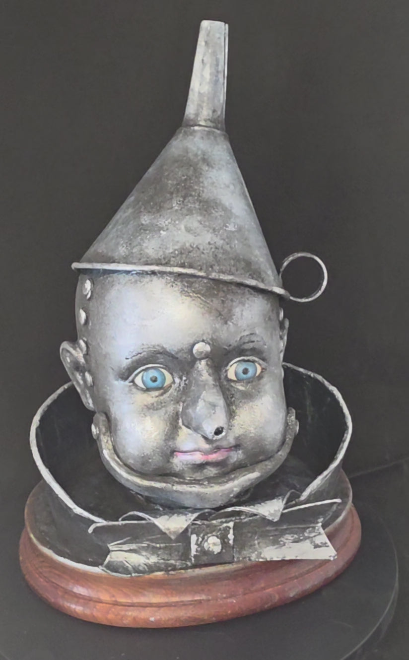 360-degree view of the Wizard of Oz Tin Man Bust sculpture, showing the aged metallic silver porcelain face, blue glass eyes, tin funnel hat, metal-like collar and bow tie details, and warm wood base from all angles